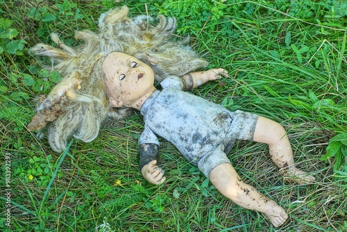 
an old, dirty  discarded children's toy small in gray clothes with a plastic face and hair, a girl's doll lies on  the green grass  during the day on the street

