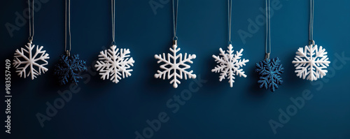 A blue background with a row of snowflakes hanging from the ceiling. The snowflakes are white and blue, and they are all different sizes and shapes. The snowflakes are arranged in a line