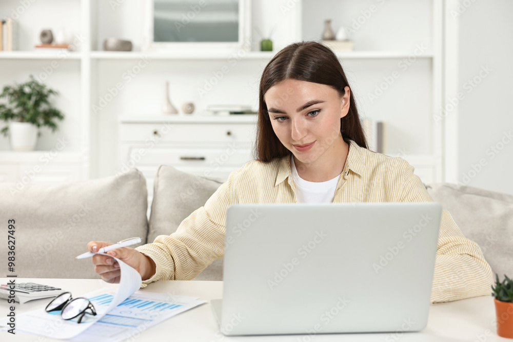 Obraz premium Budget planning. Young woman with papers using laptop at white table indoors