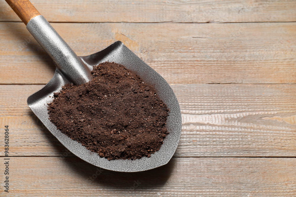 Metal shovel with soil on wooden table, space for text Metal shovel with soil on wooden table, space for text