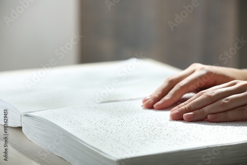 Blind woman reading book written in Braille at wooden table, closeup photo