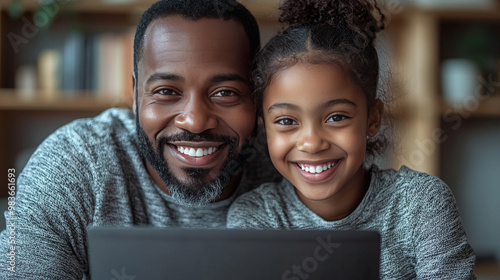 Happy father and daughter look at camera while using laptop.