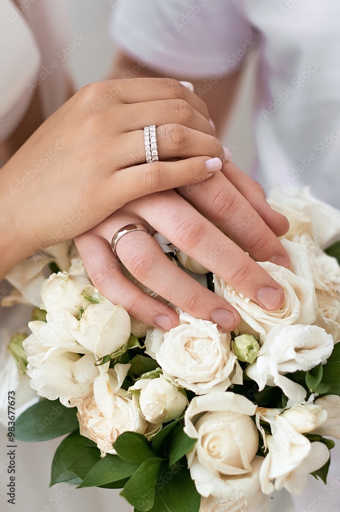 A close-up of two hands with wedding rings, holding a bouquet of white roses. A close-up of two hands with wedding rings, holding a bouquet of white roses.