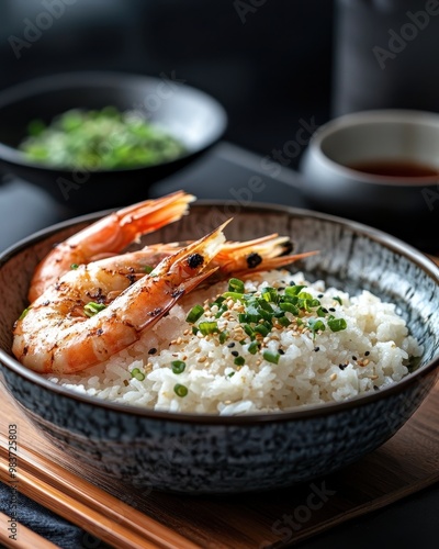 A bowl of rice topped with grilled shrimp and green onions, served in a stylish setting.