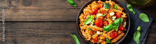 Delicious pasta dish with fresh vegetables and herbs on a wooden table.