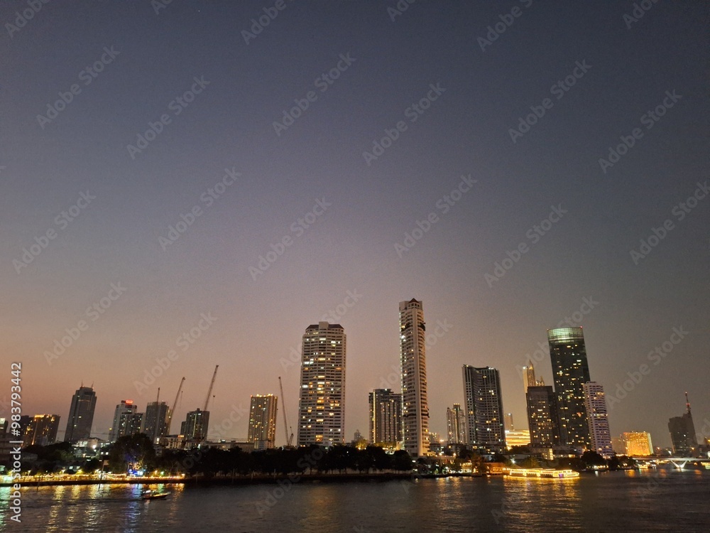 Fototapeta premium Nighttime scene of tall buildings adorned with lights by the riverside. Perfect for use as an illustration element or as a background