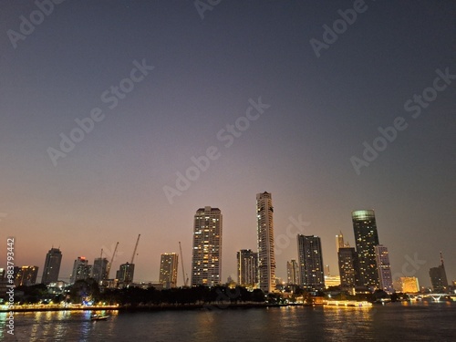 Nighttime scene of tall buildings adorned with lights by the riverside. Perfect for use as an illustration element or as a background