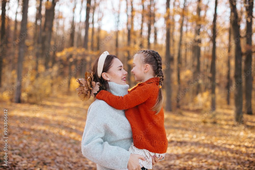 Mother is hugging her daughter with braids in an autumn forest. The woman, dressed in a gray sweater and skirt, is hugging her little daughter, who is wearing a red sweater, in the autumn forest. Mother is hugging her daughter with braids in an autumn forest. The woman, dressed in a gray sweater and skirt, is hugging her little daughter, who is wearing a red sweater, in the autumn forest.