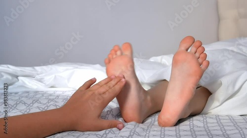 The palm tickles the child's bare feet, the feet kick and knock on the mattress. Small children play in the bed in the morning.