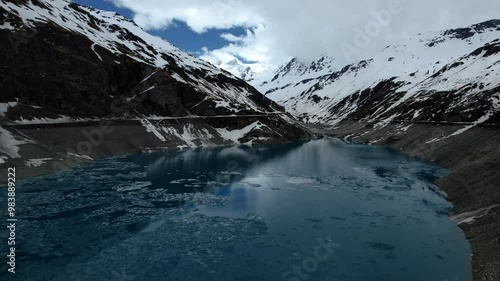 4k Drone Aerial Reverse Shot Of Vibrant Blue Glacial Water Of Lac de Moiry Dam Surrounded By Massive Snow Covered Mountains Reflecting On lake In Grimentz Switzerland photo