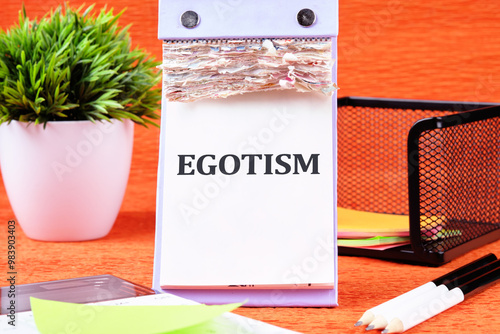 Concept image. the word EGOTISM on a blank desktop calendar page on an orange background photo