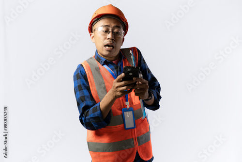 Asian adult male construction worker in full safety gear who looks very troubled carrying a smartphone and clipboard, industrial and construction concept, isolated on white background.