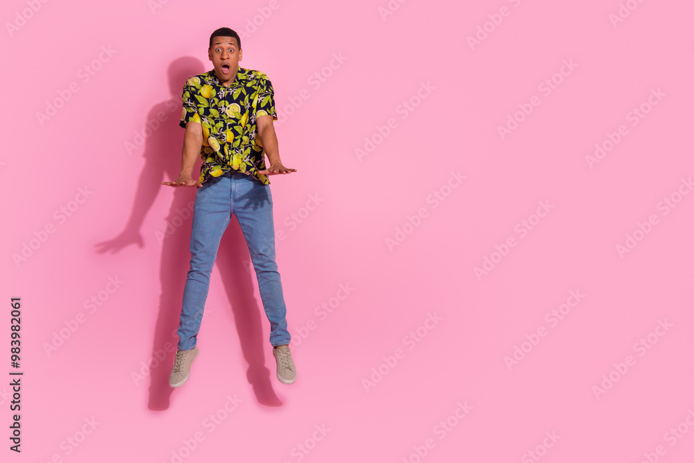 Full length photo of young guy amazed jumping pushing invisible things dressed tropical print garment isolated on pink color background Full length photo of young guy amazed jumping pushing invisible things dressed tropical print garment isolated on pink color background