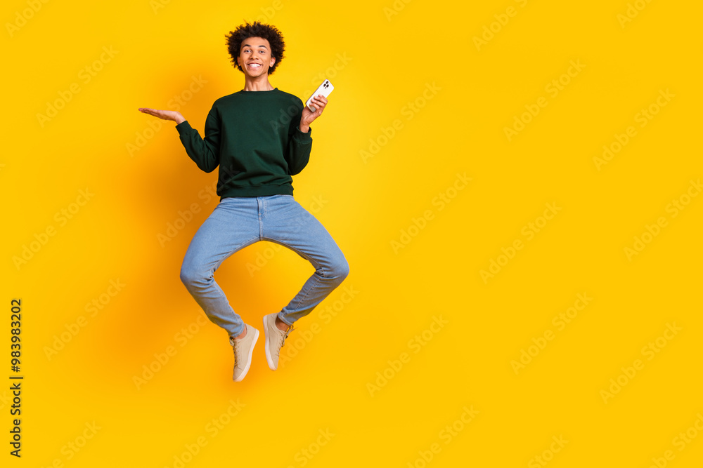 Obraz premium Full size photo of nice young man jump hold phone empty space wear pullover isolated on yellow color background