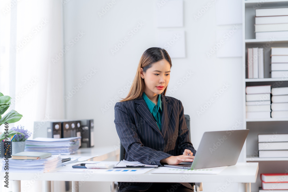 Focused Businesswoman: A professional woman in a stylish blazer and blue shirt sits at her desk, intently working on her laptop in a modern office setting, exuding confidence and dedication. Focused Businesswoman: A professional woman in a stylish blazer and blue shirt sits at her desk, intently working on her laptop in a modern office setting, exuding confidence and dedication.