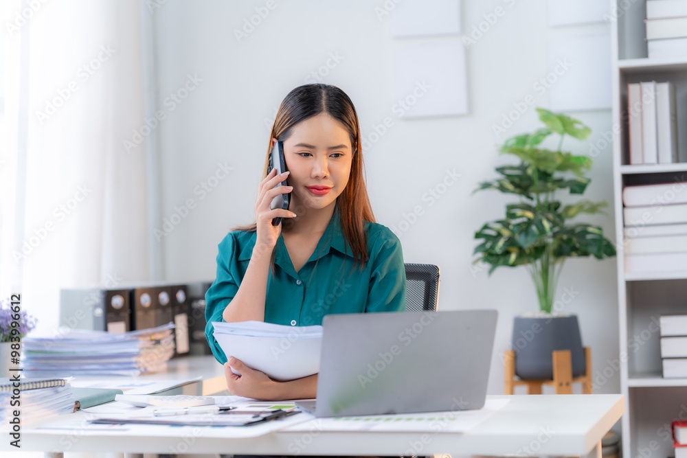 Focused and Determined: A young businesswoman, with a serious expression, navigates a demanding task, juggling phone calls and paperwork while staying organized and focused on her laptop. The image co Focused and Determined: A young businesswoman, with a serious expression, navigates a demanding task, juggling phone calls and paperwork while staying organized and focused on her laptop. The image co