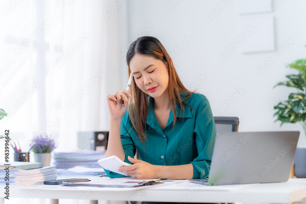Overwhelmed by Numbers: A young Asian businesswoman grapples with financial stress, her brow furrowed as she calculates expenses amidst a mountain of paperwork. Overwhelmed by Numbers: A young Asian businesswoman grapples with financial stress, her brow furrowed as she calculates expenses amidst a mountain of paperwork.