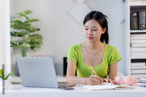 Portrait of a modern business asian woman, woman in a green shirt working on a laptop in the home office 