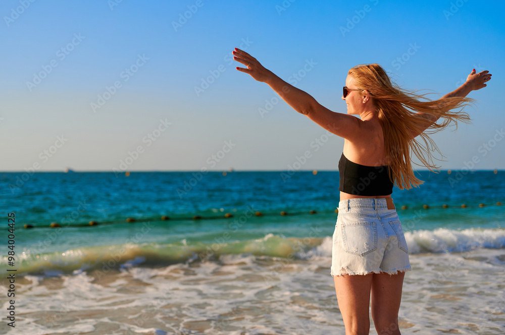 Happy woman enjoying freedom with open hands on sea. Happy woman standing on the beach with hands up. Happy woman enjoying freedom with open hands on sea. Happy woman standing on the beach with hands up.