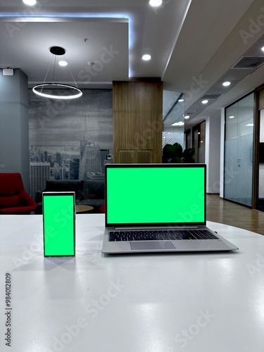a laptop and smartphone with a green screen in a spacious office
