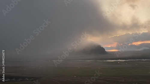 Aerial view of Mt. Petursey in Iceland at sunset, shrouded in mist with dramatic clouds and glowing light reflecting off the surrounding plains. photo