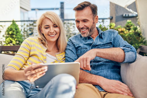 Adult couple using digital tablet at terrace sitting together on the sofa doing online shopping