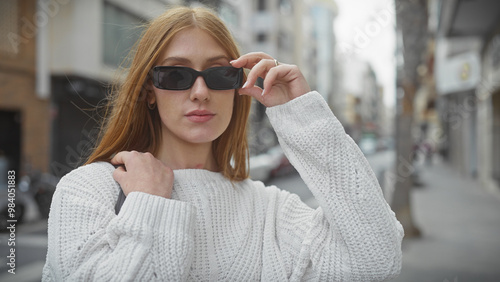 A trendy young woman adjusts her sunglasses on a city street, embodying urban fashion and youth.