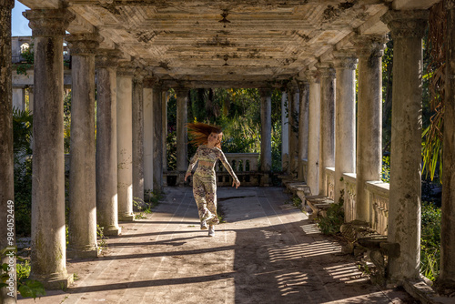 A girl is dancing in an old train station with white columns, a corridor with peeling paint on the floor and columns. An abandoned railway station in Abkhazia. A traveler with long hair