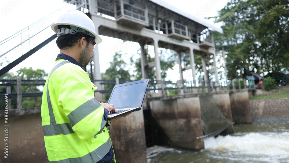 Portrait of engineer wearing green vest and white helmet with tablet Working day on a water dam with a hydroelectric power plant. Renewable energy systems, Sustainable energy concept Portrait of engineer wearing green vest and white helmet with tablet Working day on a water dam with a hydroelectric power plant. Renewable energy systems, Sustainable energy concept