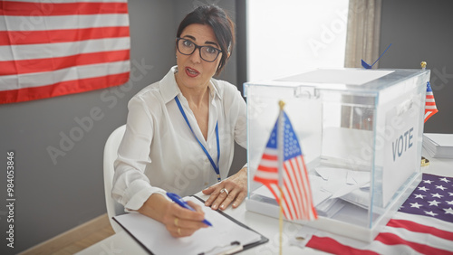 Hispanic woman supervises united states electoral process indoors with american flags and ballot box.