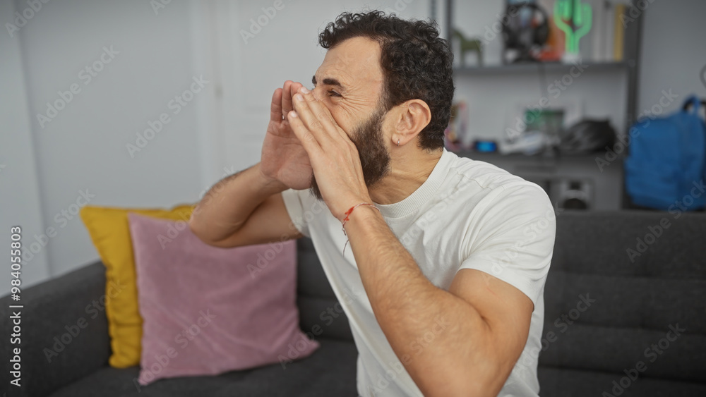 Man in white shirt sitting on couch shouting with hands cupped around mouth indoors. Man in white shirt sitting on couch shouting with hands cupped around mouth indoors.