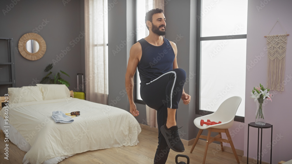 A bearded man in athletic attire exercising in a well-lit, modern bedroom, lifting his knee for a workout routine. A bearded man in athletic attire exercising in a well-lit, modern bedroom, lifting his knee for a workout routine.