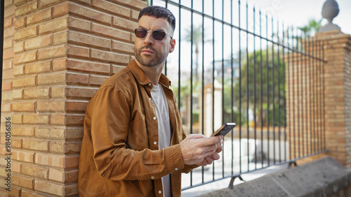 Wallpaper Mural Handsome hispanic man with sunglasses and beard using smartphone on sunny urban street. Torontodigital.ca