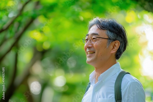 Middle-aged Japanese man in business attire, smiling while looking at camera from the side, with a blurred background of green trees in the background,generated ai.