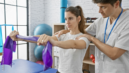 A woman patient performs physiotherapy exercises with resistance bands under the guidance of a male therapist in an indoor rehab clinic. photo