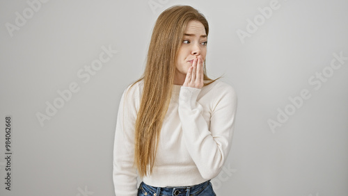 A surprised young woman with blonde hair wearing a white sweater against an isolated white background seems worried.