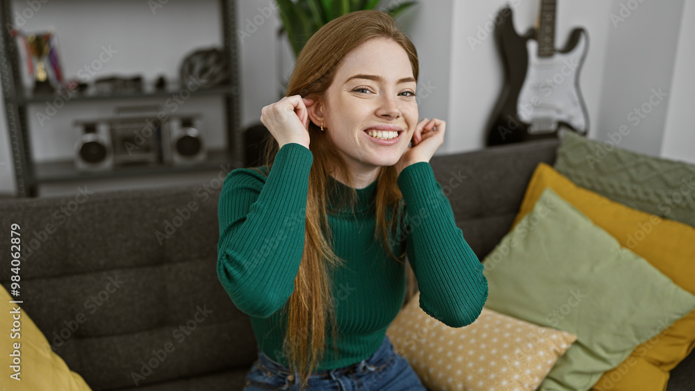 Fototapeta premium Smiling blonde woman relaxing comfortably at home on a couch with stylish pillows and guitar in the background.