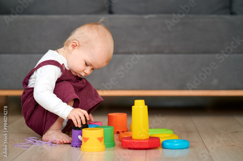 Close up Baby toddler hands plays with plastic pyramid on floor in room. Baby playing with toys, showcasing a baby engaging with the different features.