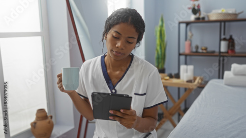 Woman relaxing at a wellness center spa holding a cup and reading on a tablet in an indoor setting, surrounded by calm and soothing decor.