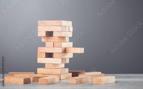 Precarious stack of wooden blocks towers on the table against a grey wall background. Symbolizes risk, uncertainty, and careful decision-making, much like in a game of balancing strategy and chance photo