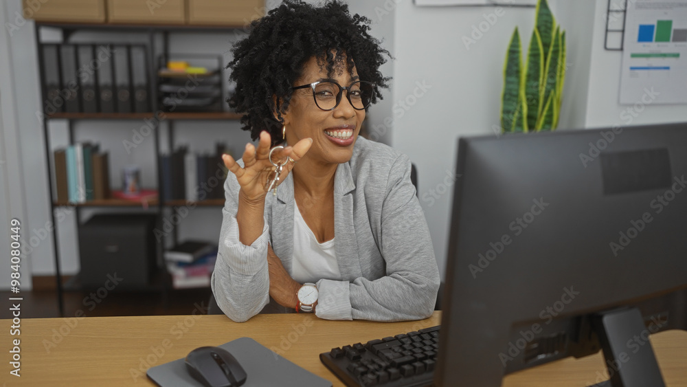 A beautiful young african american woman with curly hair works in an office, smiling while holding keys and sitting at a desk with a computer. A beautiful young african american woman with curly hair works in an office, smiling while holding keys and sitting at a desk with a computer.