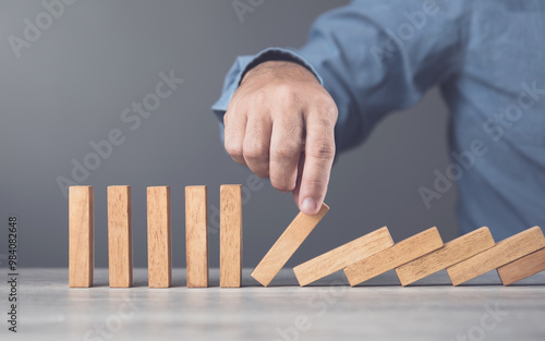 Businessman uses his hand stopping wooden blocks from falling, representing the domino effect and risk management. Symbolizes taking action to prevent cascading problems and managing risks effectively photo