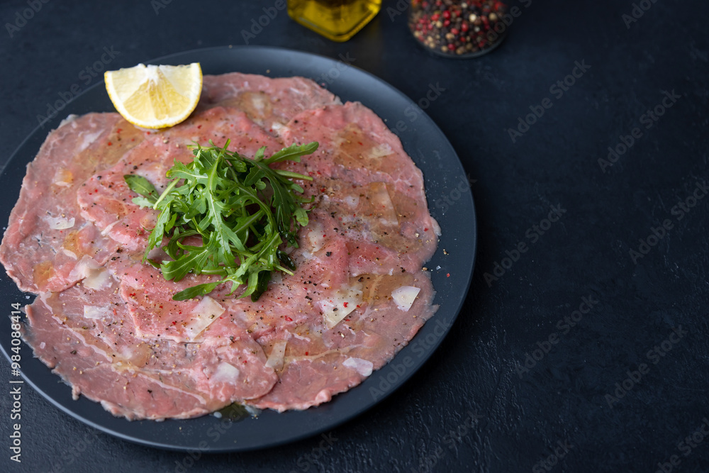 Marbled beef carpaccio with arugula, parmesan cheese, olive oil and lemon. A traditional classic appetizer made from thinly sliced raw meat. Close-up, selective focus, black background. Marbled beef carpaccio with arugula, parmesan cheese, olive oil and lemon. A traditional classic appetizer made from thinly sliced raw meat. Close-up, selective focus, black background.