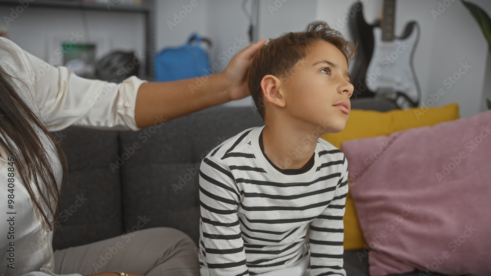 Obraz premium A caring woman gently touches a thoughtful boy's head in a cozy, well-furnished living room, expressing familial love.