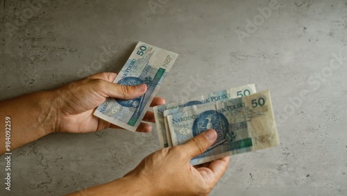 Hands holding and exchanging polish zloty bills on a concrete background, depicting a financial transaction or payment.