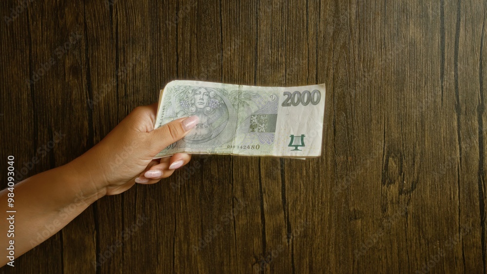 Woman holding 2000 czech koruna note with hand and polished nails against wood background Woman holding 2000 czech koruna note with hand and polished nails against wood background