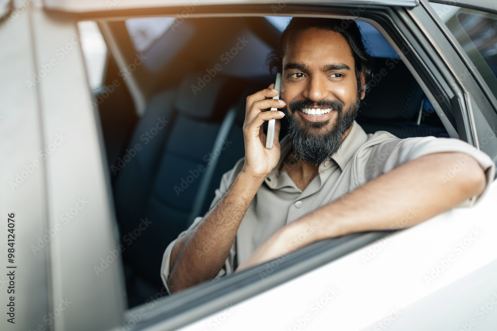 A cheerful man leans out of a car window, enjoying a phone conversation while basking in the sunlight. His relaxed demeanor adds to the vibrant atmosphere of the day. A cheerful man leans out of a car window, enjoying a phone conversation while basking in the sunlight. His relaxed demeanor adds to the vibrant atmosphere of the day.