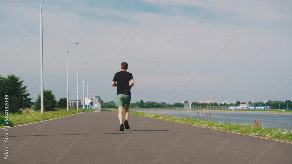 A young man jogs along the riverbank in summer, enjoying fitness amid nature. His effort and determination reflect a healthy lifestyle and positive mindset, embracing freedom in the outdoors A young man jogs along the riverbank in summer, enjoying fitness amid nature. His effort and determination reflect a healthy lifestyle and positive mindset, embracing freedom in the outdoors