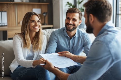A smiling couple sitting together on a couch with the man handing over a document