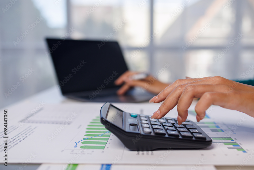 Close up of female hand accountan using a laptop computer and calculator to calculate taxes at desk in the office financial business, calculating accounting online marketing. Close up of female hand accountan using a laptop computer and calculator to calculate taxes at desk in the office financial business, calculating accounting online marketing.